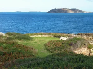 Vue sur la mer depuis la Pointe de Port-L'Épine à Trélévern, avec des vestiges de murs en pierre entourés de landes côtières et les îles en arrière-plan, Côtes-d'Armor, Bretagne